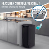 Eine moderne Küche mit einem schwarzen WELLENBORG Pfandflaschen-Sammelbehälter (100l, 2 Tragetaschen, Klettverschluss) zur Aufbewahrung von Flaschen. Eingefügt: Behälter gefüllt mit Plastikflaschen. Text: Flaschen stilvoll verstaut – Für mehr Effizienz und Ordnung.