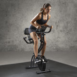 FitEngine Heimtrainer mit Expanderbändern - schwarz, Frau trainiert auf höhenverstellbarem Sattel mit großem Display und Pulsensoren.