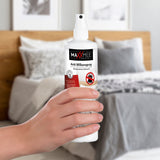 Hand hält MAXXMEE Anti-Milbenspray - 250 ml vor Bett, ideal gegen Hausstaubmilben auf Matratzen und Polstermöbeln.