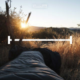 Where Tomorrow Camping Schlafsack Small & Light in Goblinblau liegt draußen bei Sonnenaufgang in der Natur.