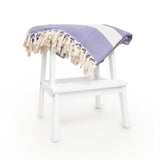 LUMALAND Baumwolldecke / Tagesdecke aus 100 % Baumwolle, ca. 200 x 240 cm, lila mit Fransen auf weißem Hocker.