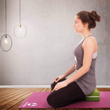 Frau sitzt in Meditationshaltung auf dem #DoYourYoga Yogablock Damodar 28x20x5 cm rot, auf Yogamatte in hellem Raum.