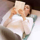 Frau liegt entspannt auf dem #DoYourFitness Akupressur-Set Bikash mit Massagematte und Kopfkissen in Blau und liest ein Buch.