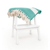 LUMALAND Baumwolldecke / Tagesdecke aus 100 % Baumwolle - ca. 200 x 240 cm - Grün liegt gefaltet auf weißem Hocker