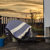 LUMALAND Baumwolldecke / Tagesdecke aus 100 % Baumwolle - ca. 200 x 240 cm - Marineblau liegt auf schwarzem Stuhl im Außenbereich bei Sonnenuntergang.