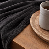 LUMALAND Kuscheldecke - 150x200 cm - weiche, schwarze Sofadecke aus Coral-Fleece neben einer Kaffeetasse auf Holzplatte.
