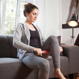 Frau nutzt #DoYourFitness Massageroller Murali 41cm lang Schwarz/Grün zur Selbstmassage der Beinmuskulatur auf Sofa.