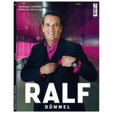 Ein Mann in dunklem Anzug und rosa Hemd lächelt auf einem Zeitschriftencover mit dem Titel „RALF DÜMMEL“.