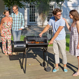 GRILLCHEF Holzkohlegrill Smoker - 116cm - schwarz im Garten mit Rauch und Grillgut, ideal für gemütliches Grillen im Freien.