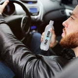 Mann im Auto hält eine Flasche FLOWKISS Koffeinhaltiges Wasser - 12er-Set mit Zitronengeschmack, kalorien- und zuckerfrei.