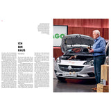 Ein Mann steht neben einem silbernen Auto mit geöffneter Motorhaube und spricht in einen Fernseher. Auf der linken Seite ist Text zu sehen.