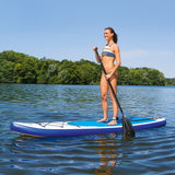 EASYmaxx Stand-Up Paddle-Board mit Zubehör in weiß/blau auf dem Wasser, Paddel und Finnen sichtbar, Frau steht auf Board