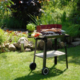 GRILLCHEF Holzkohlegrill Grillwagen - 87cm schwarz/rot mit emaillierter Feuerschüssel, Ablagetisch und verchromtem Grillrost im Garten.