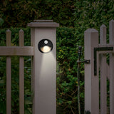 MAXXMEE LED-Sensorlicht mit Bewegungsmelder und Erdspieß, rund, 2er-Set, grau, witterungsbeständig und kabellos am Gartenzaun montiert.