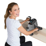 Frau trainiert mit VITALmaxx Mini-Trainer mit Metallschwungrad - grau/schwarz zur Stärkung von Arm- und Beinmuskulatur am Tisch.