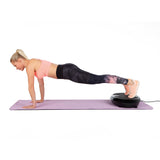 Frau macht Liegestütze mit Füßen auf VITALmaxx Vibrationstrainer rund 200W schwarz auf Yogamatte zuhause.