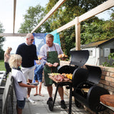 LANDMANN Smoker Vinson 200 - schwarz mit 16 Zoll Garkammer, Feuerbox, Edelstahlgriffen und Deckelthermometer beim Grillen im Garten.