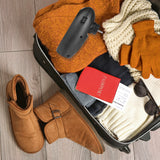 EASYmaxx Mini-Heizung Kamin-Optik 400W schwarz neben gepacktem Koffer mit Winterkleidung, Handschuhen und Stiefeln.