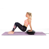 Frau trainiert zu Hause mit VITALmaxx Vibrationstrainer rund 200W schwarz auf lila Matte für Ganzkörpertraining.