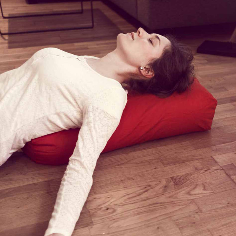 Frau entspannt auf rotem #DoYourYoga Yoga-Bolster Paravati, 67 x 22 x 13 cm, gefüllt mit Bio-Dinkelspelz, ideal für Yin Yoga.